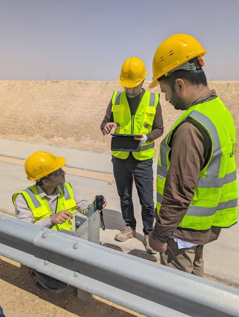 Four-person field team at the Qiddiya guardrail testing site, with desert terrain and roadway barrier visible